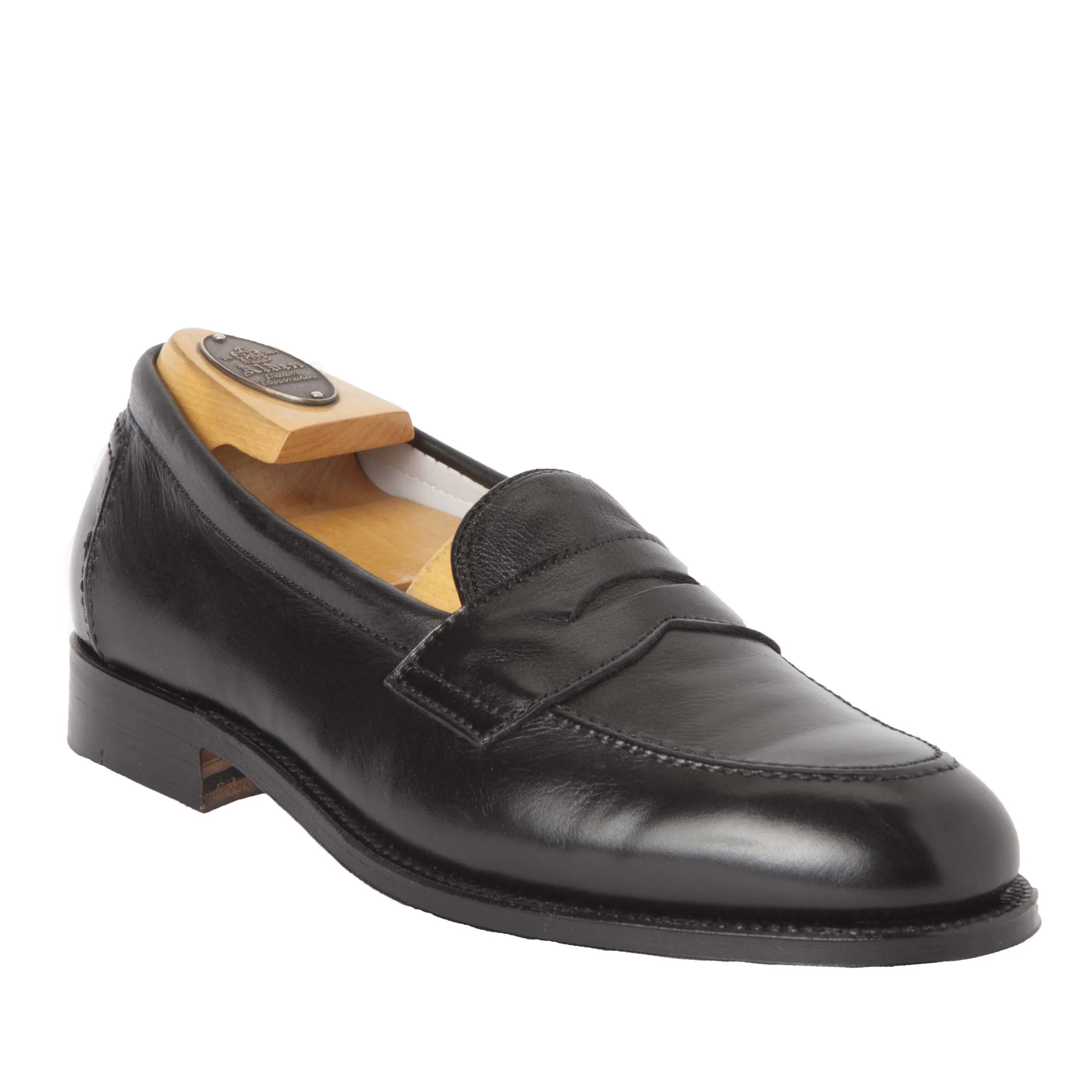 The Alden 9695F Flex Penny Loafer in Black Calfskin features a black leather finish, crafted with the Copley Last, smooth finish, penny strap, low heel, and a comfortable Flex Leather Sole. A wooden shoe tree is displayed inside.