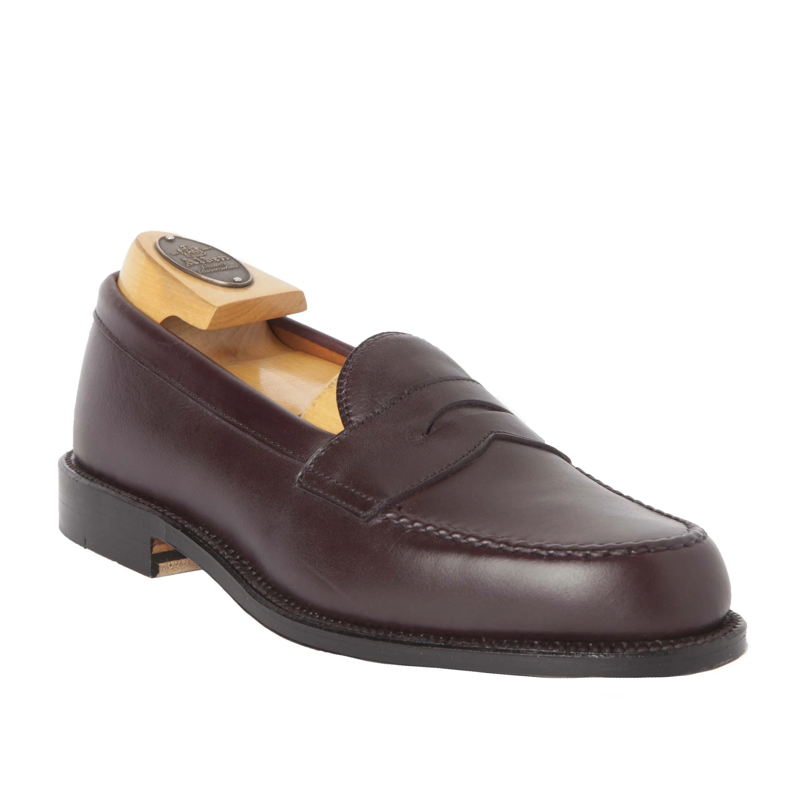 A single burgundy calfskin loafer by Alden Madison, crafted in a Van Last silhouette, is displayed at an angle with a wooden shoe tree. Featuring a penny slot, it has an oak leather sole and polished finish for timeless elegance. Product Name: 984 - Leisur