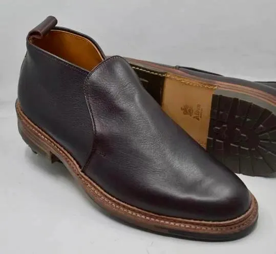 The Alden Madison D2714C - 750 Slip On Chukka in Arabica Lux features dark brown leather, a rounded toe, tan leather lining, and a sturdy Commando Rubber Sole. One shoe stands upright while the other displays its sole on a light surface.