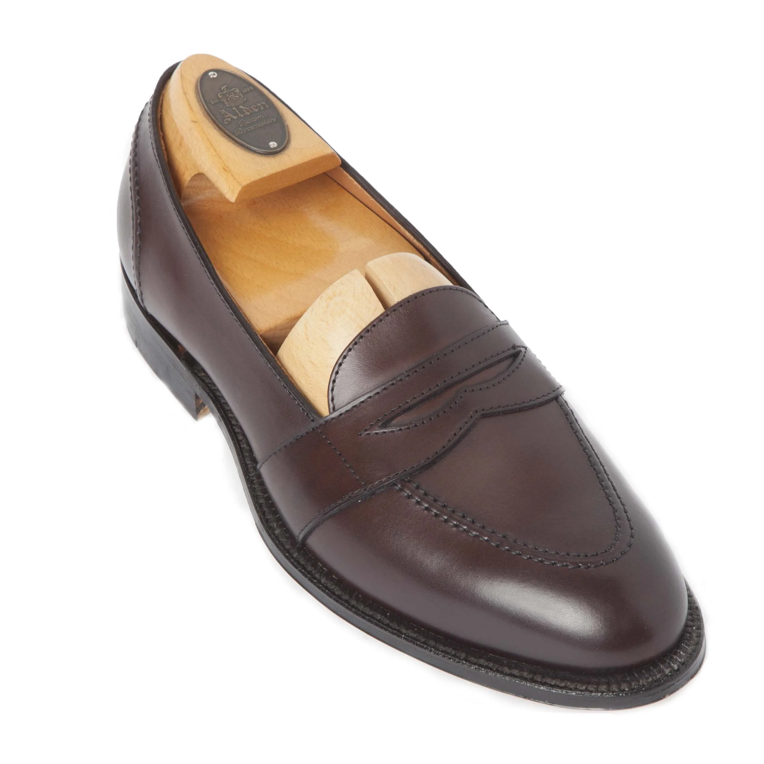 The 686 Full Strap Loafer in brown calfskin by Alden Madison, crafted on the Aberdeen Last, boasts a sleek design with visible side stitching and a smooth finish. Inside, a wooden shoe tree engraved on the knob helps maintain its shape.