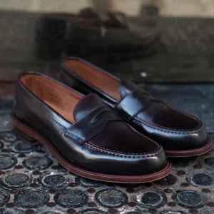 A pair of D6207 - Antique LHS in Color 8 Shell penny loafers from Alden Madison sits on a textured black rubber mat, highlighting their sleek design, leather sole, and light tan interior. The shoes feature intricate antique edging and detailed stitching, r