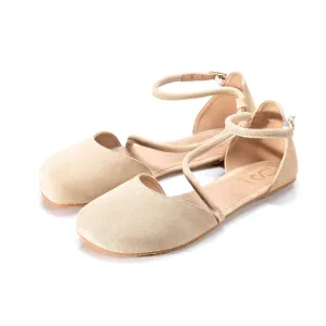 A photo of Beige Shapen Orchid flats.  Shoes are suede with tan rubber soles. A toe box and heel cup bookmark each end of the shoe with a round strap that zig zags from the toe box to the ankle/heel cup to keep the shoes secured to the foot. Both shoes are